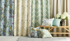Skräddarsydda gardiner och prydnadskuddar av gardintyger i olika färg och mönster i ett rum. 