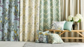 Uppsydda gardiner och prydnadskuddar av gardintyger i olika färg och mönster i ett rum. 