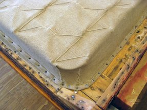 Ett kraftigt väv av linne har laggts på ett resårhus och spikats fast på stommen. Resårerna har sytts fast på linneväv på ett traditionellt vis.